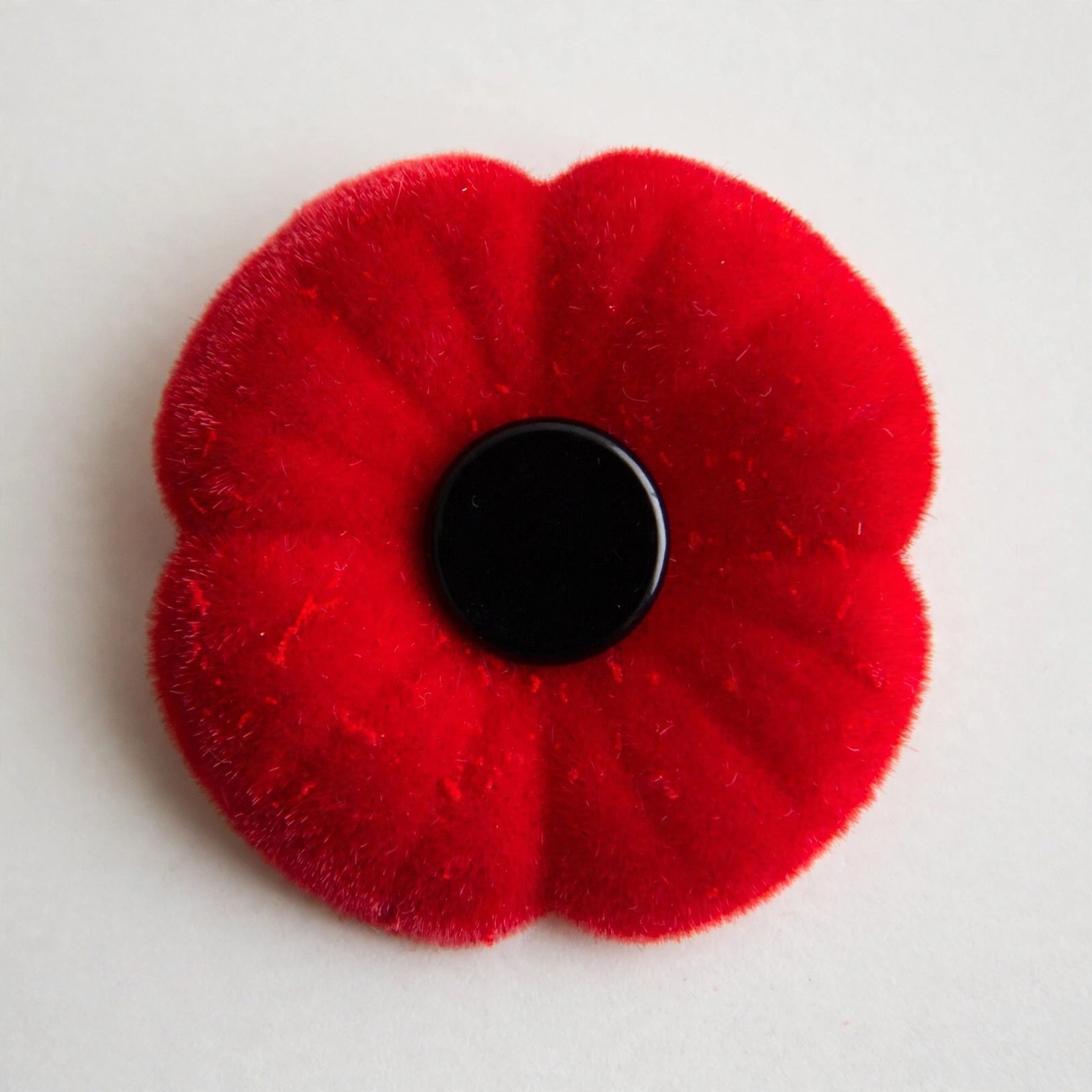 A Canadian Royal Canadian Legion remembrance poppy pin, with four red flocked petals and a flat black centre, no leaf, no pin sticking out