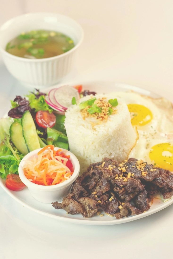 A silog brunch plate with two fried eggs, garlic rice, atchara, salad and a cup of soup
